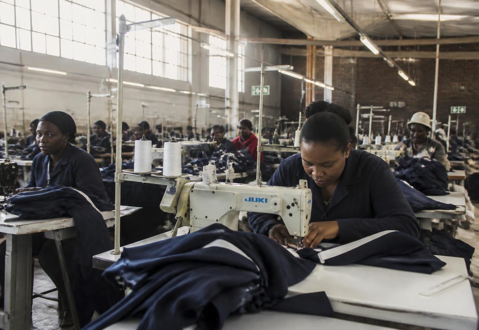 Machinists sewing navy tracksuit panels on industrial machines inside the Bee Apparel factory in Selby, Johannesburg